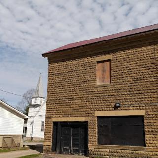An old brick building with a boarded-up window under a cloudy sky.