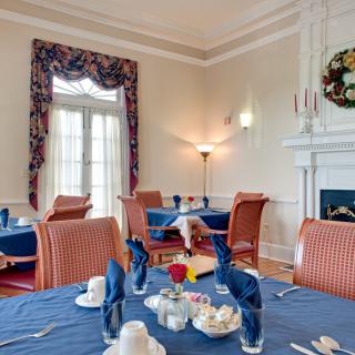 An elegantly set dining room with blue tablecloths and neatly folded napkins, featuring a cozy fireplace and classic interior design.