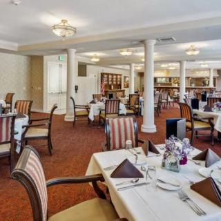 An elegantly decorated dining room with neatly arranged tables and chairs, and chandeliers overhead.