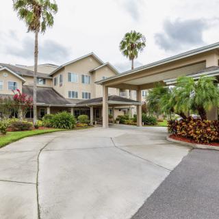 A residential building with a covered driveway, surrounded by palm trees and landscaping under an overcast sky.