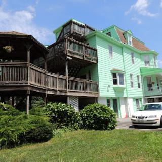 A two-tone green house featuring balconies and surrounded by greenery.