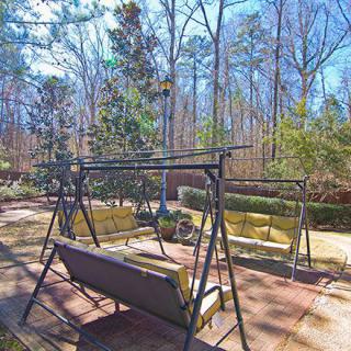 A sunny backyard features swings and garden furniture surrounded by trees.