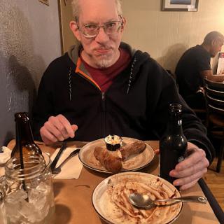 A man enjoying a meal at a cozy restaurant, featuring dessert on the table.