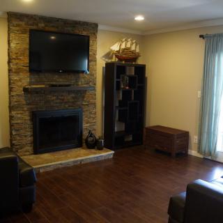 A cozy living room featuring a stone fireplace, mounted television, and hardwood flooring.