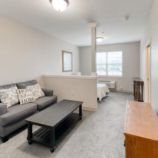A cozy living room with a grey sofa, coffee table, and a window providing natural light.