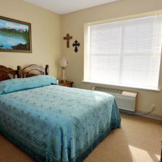 A cozy bedroom with a blue bedspread, wall decor, and a large window letting in natural light.