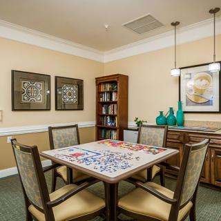 A cozy room with a table set for games, surrounded by chairs, artwork on the walls, and a bookshelf.