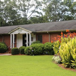 A charming brick house surrounded by vibrant gardens and lush greenery.