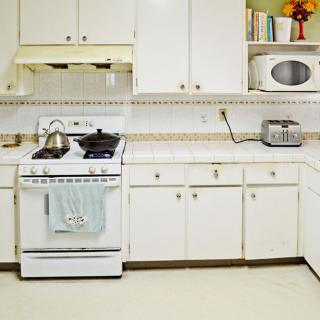A kitchen featuring white cabinets, a stove, microwave, and toaster on the countertop.