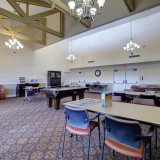 A spacious recreation room with a billiards table, chairs, and tables under elegant chandeliers.