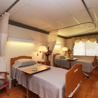 A shared hospital room equipped with two beds, bedside tables, and natural light streaming through the window.