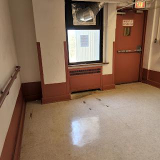 An empty hallway featuring a door and window, characterized by simple flooring and wall decor.