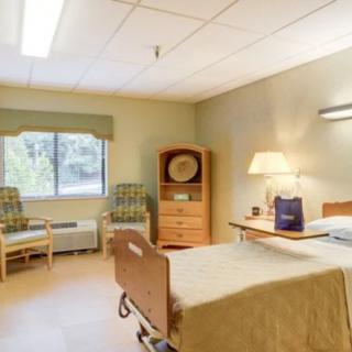 A clean and quiet hospital room with a bed, seating area, and natural light from a window.