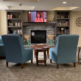A cozy living room with two armchairs facing a fireplace, bookshelves, and a television mounted above.