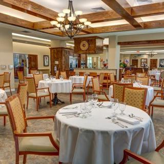 An elegant dining room with neatly arranged tables and chairs, featuring warm decor and soft lighting.