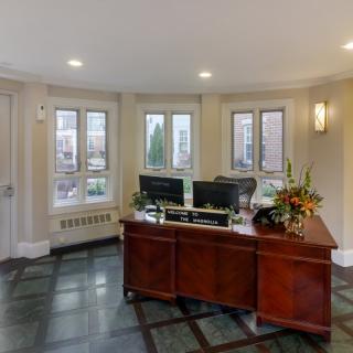 A well-lit office reception area featuring a wooden reception desk with computer monitors and floral decorations.