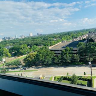 A panoramic view of a city skyline surrounded by greenery under a clear blue sky.