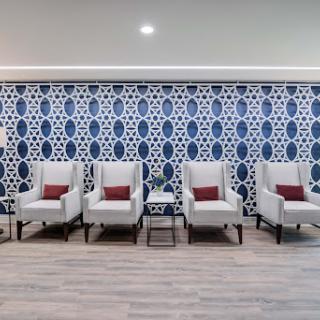 A modern waiting area featuring stylish white chairs with red cushions against a beautifully patterned blue and white wall.