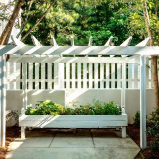 A garden area with a pergola and planter box, set against a white fence.