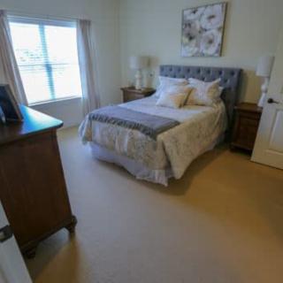A cozy bedroom with a neatly made bed, nightstands on each side, a dresser, and a large window.