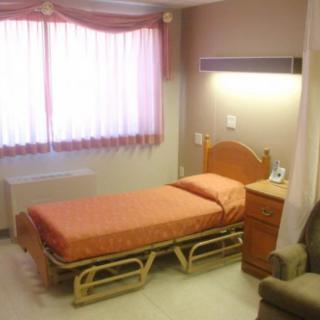 A simple hospital room with a single bed and bedside furniture.