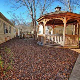 A wooden gazebo in a yard covered with autumn leaves.