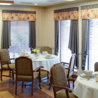 A cozy dining room with tables set for a meal, featuring large windows and elegant curtains.