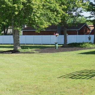 A well-maintained backyard with a green lawn, trees, and a white fence.