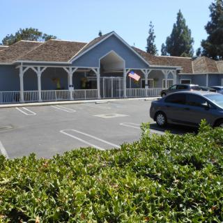 A building with a parking lot and a car parked, surrounded by trees and bushes on a sunny day.