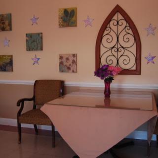 A cozy corner featuring a wooden table and chair adorned with flowers, complemented by decorative wall art.