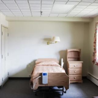A minimalist hospital room with a single bed and basic furniture.