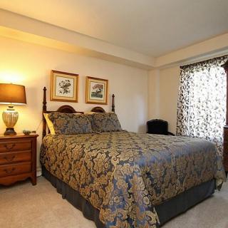 A cozy bedroom with a neatly made bed, bedside table, and a lamp by the window.