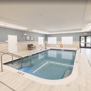 A clean and well-lit indoor swimming pool area with seating and safety equipment.