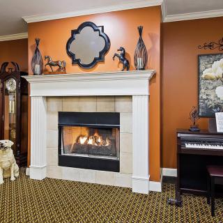 A cozy living room featuring a fireplace with decorative elements and a piano against a warm-toned wall.