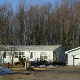 A single-story house with a garage, surrounded by leafless trees and patches of snow.