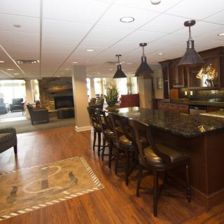A modern kitchen with an open floor plan featuring a bar area with stools, pendant lighting, and hardwood floors.