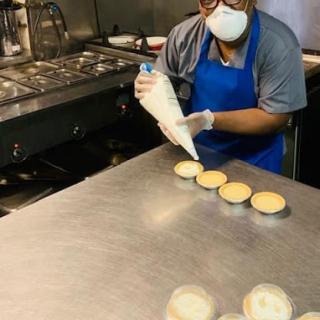 A chef is skillfully piping frosting onto cupcakes in a busy kitchen.