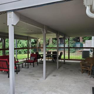 A cozy outdoor patio featuring a variety of seating options under a covered structure, surrounded by lush greenery.