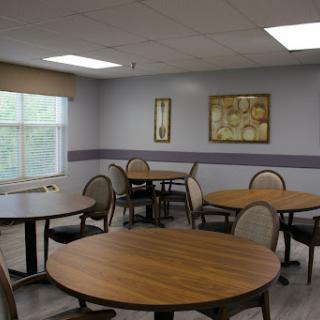 A cozy dining area featuring round wooden tables and comfortable chairs, illuminated by natural light from a nearby window.