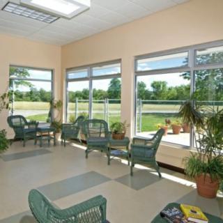 A bright and airy waiting area with large windows, wicker chairs, and lush plants overlooking a scenic outdoor view.