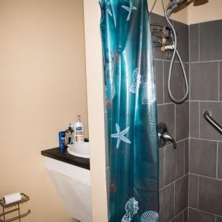 A bathroom with a tiled shower area featuring a blue shower curtain, a sink, and various toiletries.