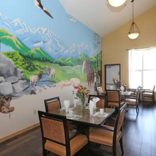 A cozy dining room featuring a vibrant nature-themed mural with mountains and forests, accompanied by elegantly set tables and chairs.