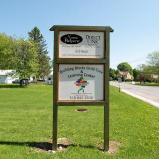 A community center sign displaying information about local services and activities, set against a clear blue sky and green surroundings.