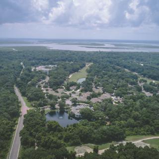 Aerial view of a lush green landscape with roads, lakes, and a cloudy sky.