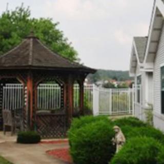 A charming garden scene featuring a wooden gazebo, well-manicured bushes, and a white fence.
