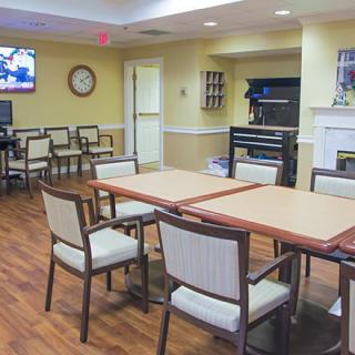 A meeting or common room with tables and chairs, equipped with a television and clock on the wall.