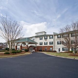 A large residential building with a paved driveway and surrounding trees under a cloudy sky.