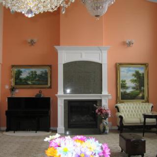 A cozy living room with a fireplace, piano, chandelier, and floral decorations.