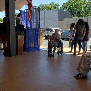 A group of people, including someone in a wheelchair, gathered near a doorway with sunlight streaming in.