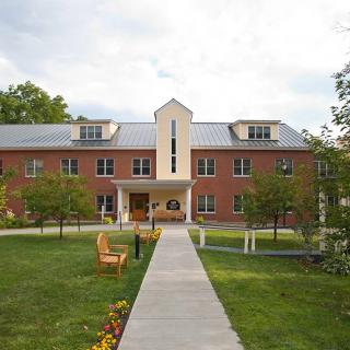 A brick building on a campus with a pathway and benches in the foreground, surrounded by trees.